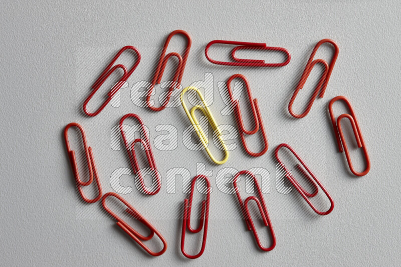 A bunch of red paper clips with a different colored paper clip in the center on grey background