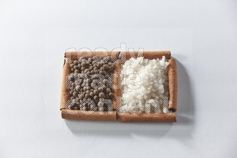 مربعان من أعواد القرفة ممتلئان بالملح الأبيض وحبوب الفلفل الحلو علي خلفية بيضاء