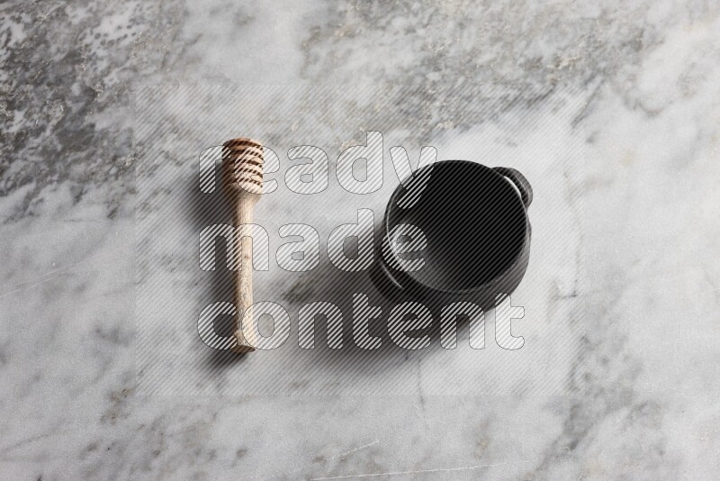 Black pottery bowl with wooden honey dipper on the side on grey marble background