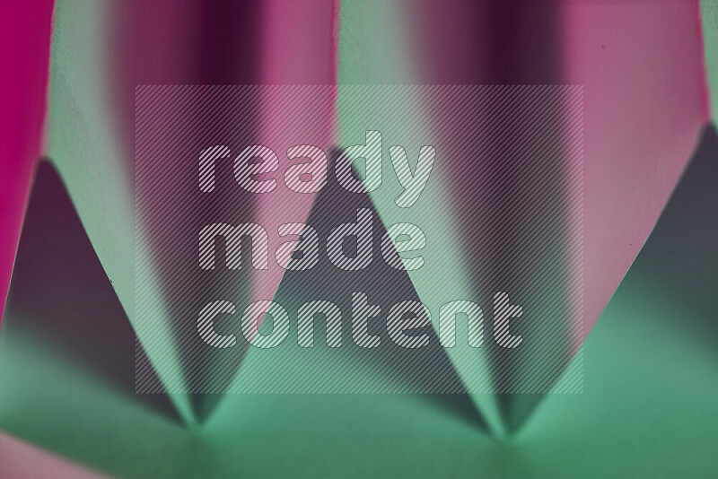 A close-up abstract image showing sharp geometric paper folds in green and pink gradients