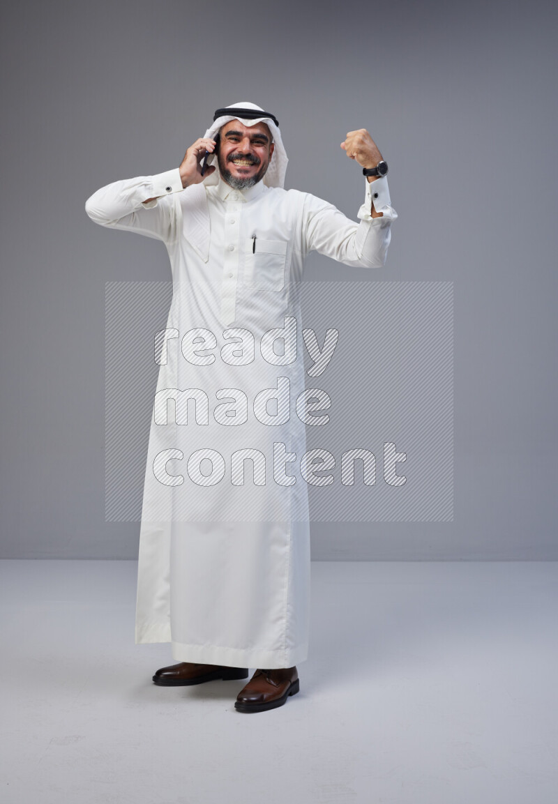 Saudi man Wearing Thob and white Shomag standing talking on phone on Gray background