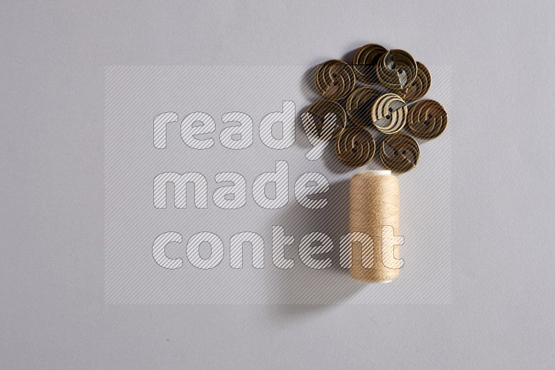 A beige sewing thread spool with colored buttons on grey background