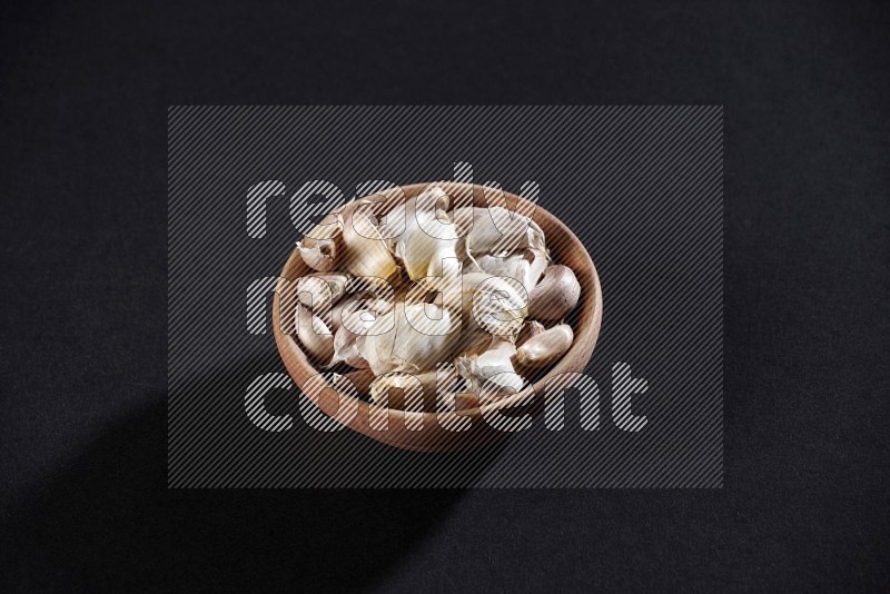 A wooden bowl full of garlic cloves on a black flooring