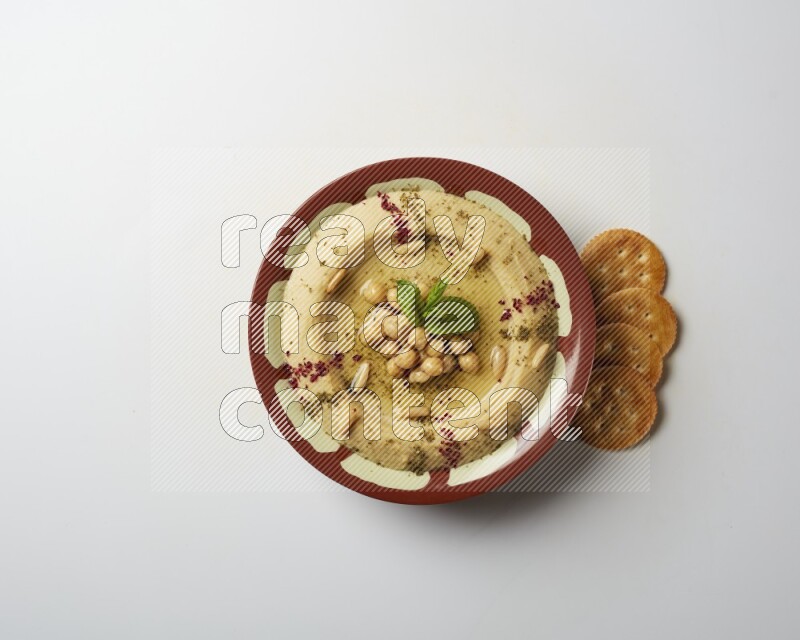Hummus in a traditional plate garnished with zaatar & sumak on a white background