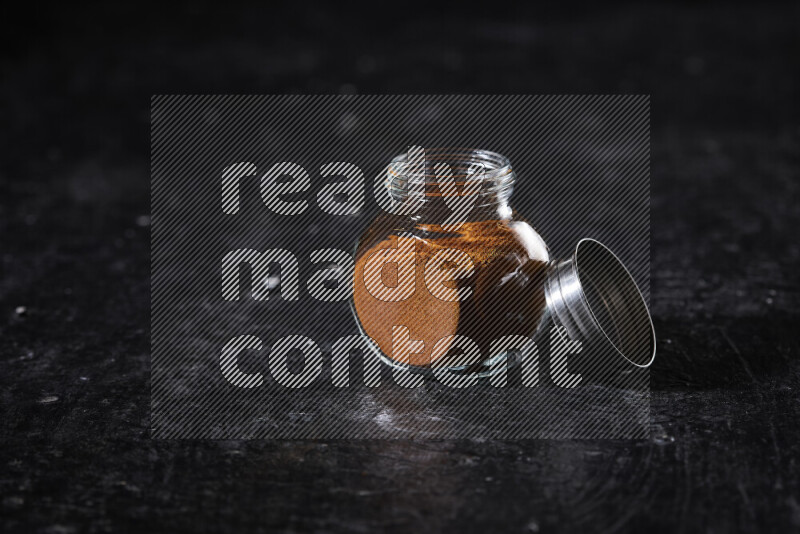 A glass jar full of ground paprika powder on black background