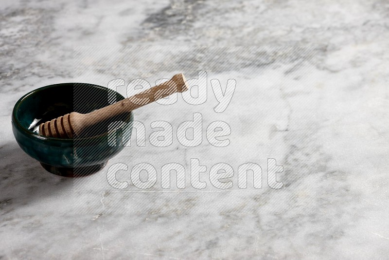 Dark green Pottery Plate with wooden honey handle in it, on grey marble flooring, 45 degree angle