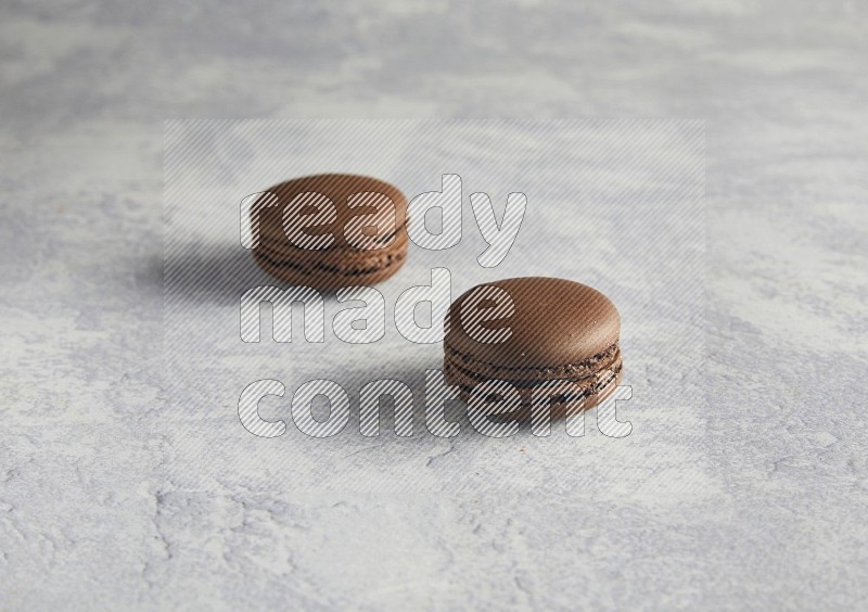 45º Shot of two Brown Dark Chocolate macarons  on white  marble background