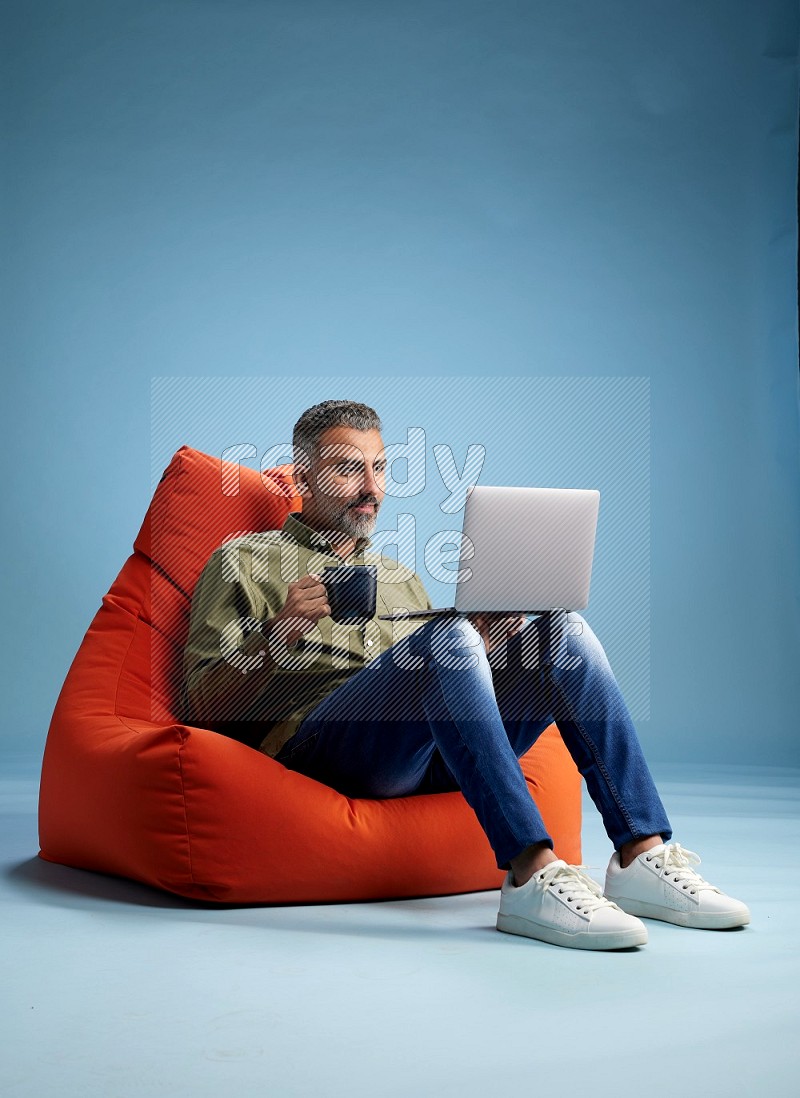 A man sitting on an orange beanbag and working on laptop