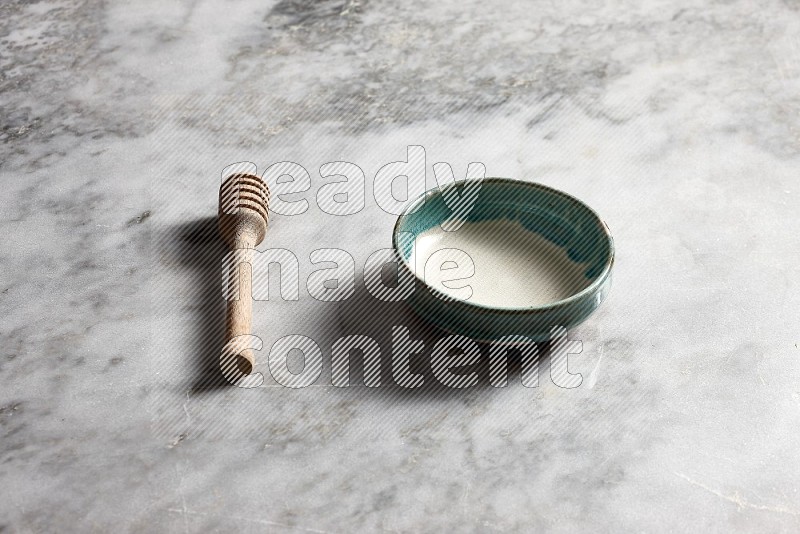 Multicolored Pottery bowl with wooden honey handle on the side with grey marble flooring, 45 degree angle