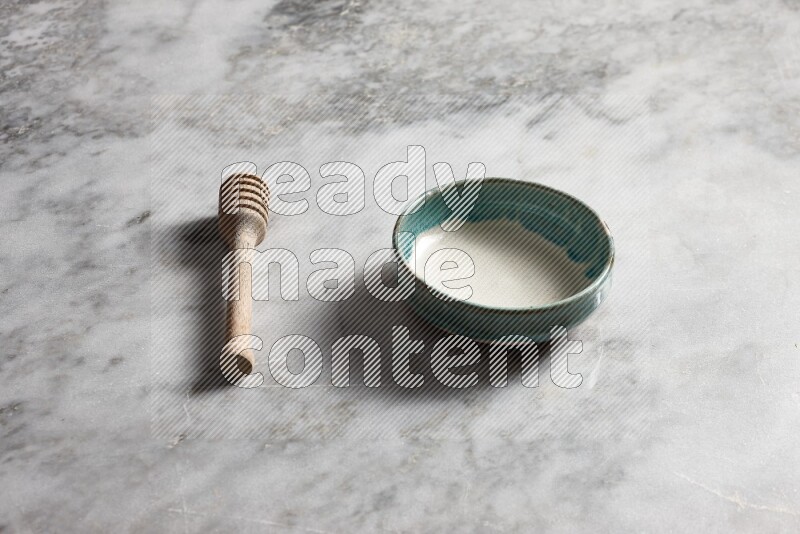 Multicolored pottery bowl with wooden honey dipper on the side on grey marble background