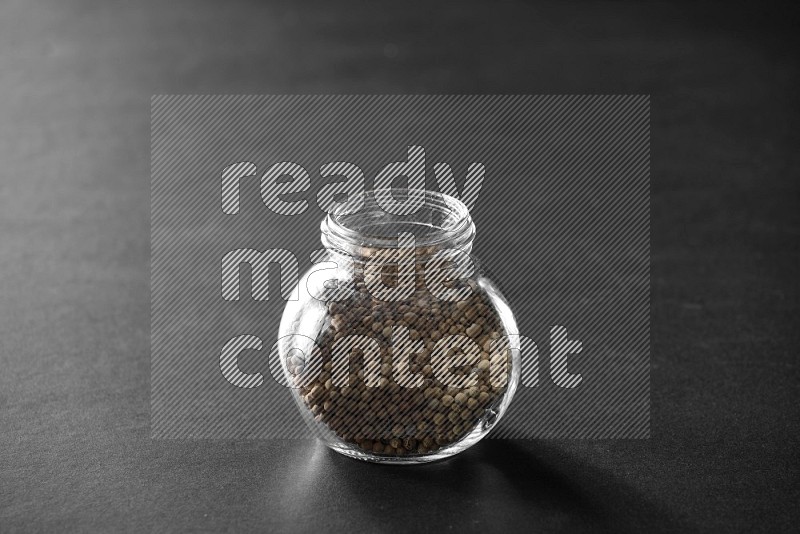 A glass spice jar full of white peppers on black flooring