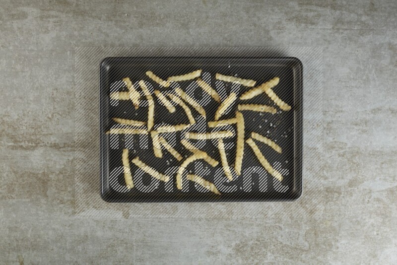crinkle fries in a black stainless steel rectangle tray on grey textured counter top