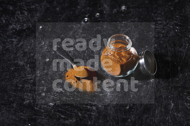 A glass jar full of ground paprika powder on black background