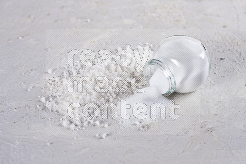 A glass jar full of table salt with some sea salt crystals beside it on a white background