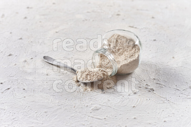 A glass jar full of onion powder flipped with some spilling powder on white background