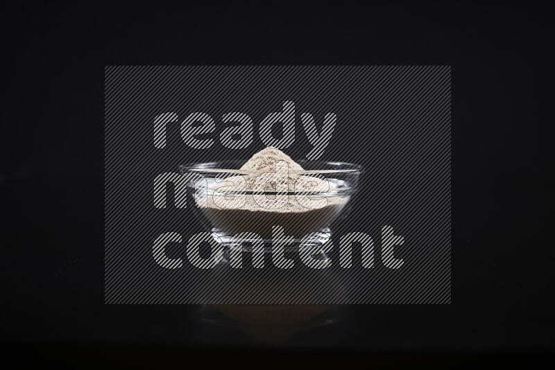 A glass bowl full of onion powder on black background