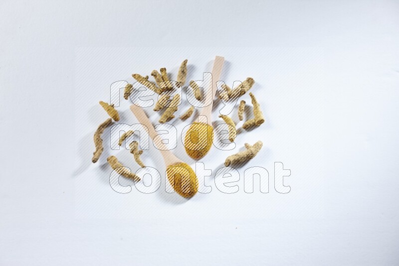2 wooden spoons full of turmeric powder with dried turmeric fingers beside it on white flooring