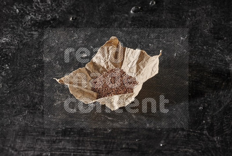 A crumpled piece of paper full of flaxseeds on a textured black flooring