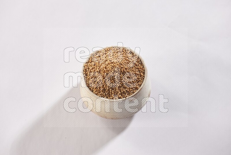 A beige pottery bowl full of mustard seeds on white flooring