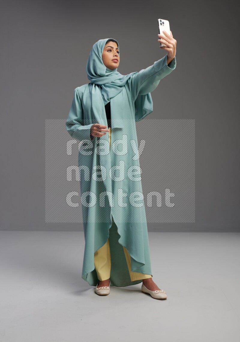 Saudi Woman wearing Abaya standing taking selfie on Gray background