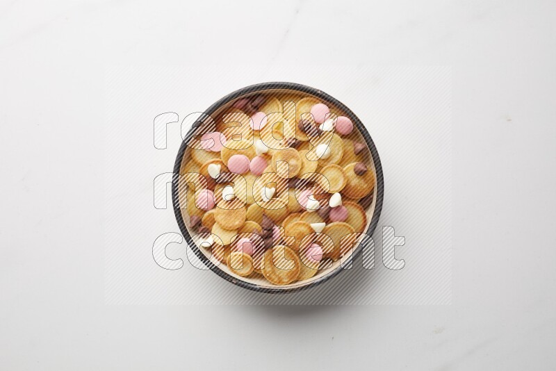 Top-view shot of mixed chocolate chips cereal pancakes in a round bowl on white background