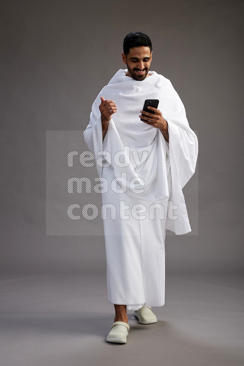 A man wearing Ehram Standing texting on phone on gray background