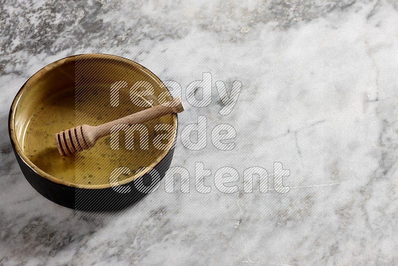 Multicolored Pottery Oven Plate with wooden honey handle in it, on grey marble flooring, 65 degree angle