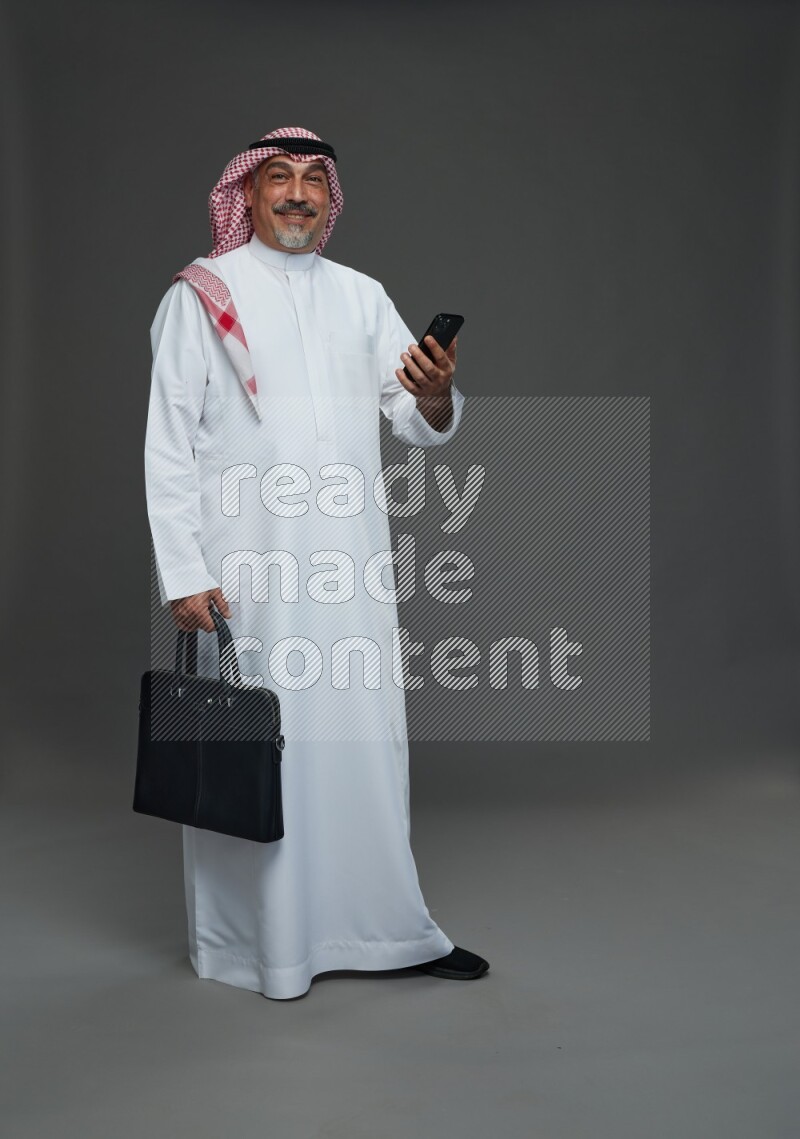 Saudi man with shomag Standing holding bag and phone on gray background