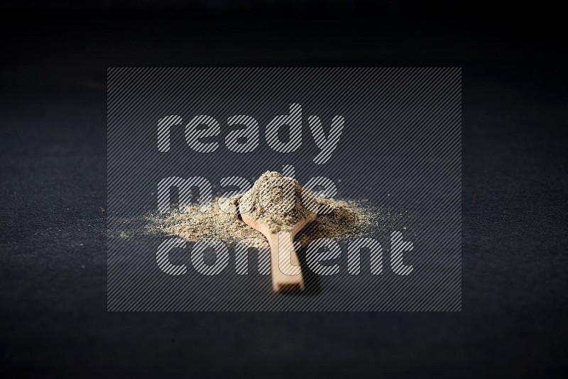 A wooden spoon full of cardamom powder and powder spreaded on black flooring