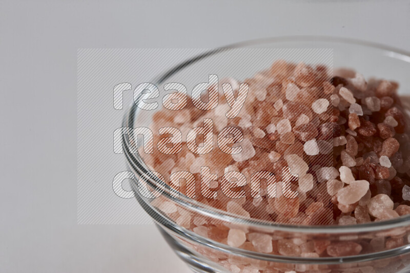 A glass bowl full of coarse himalayan salt crystals on white background