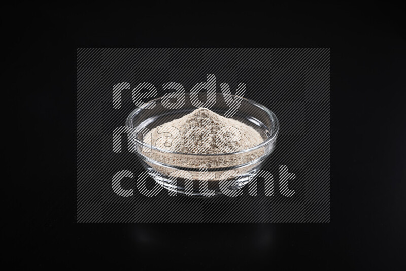 A glass bowl full of onion powder on black background