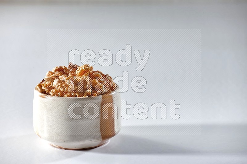 A beige ceramic bowl full of peeled walnuts on a white background in different angles