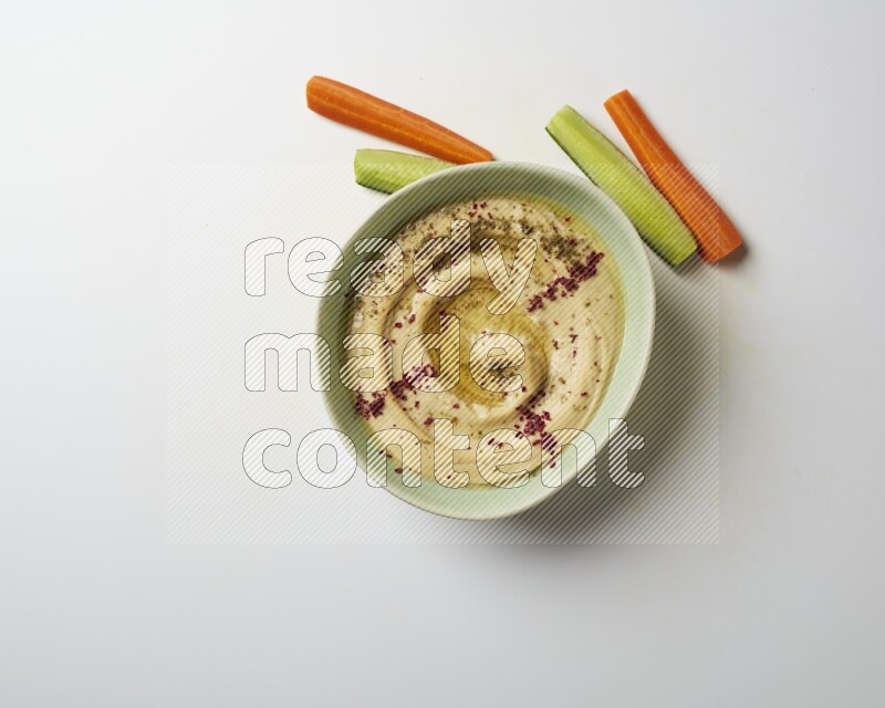 Hummus in a green plate garnished with zattar & sumak on a white background