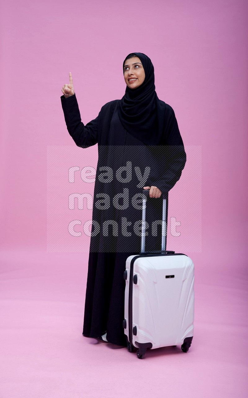 Saudi woman wearing Abaya standing holding bag on pink background