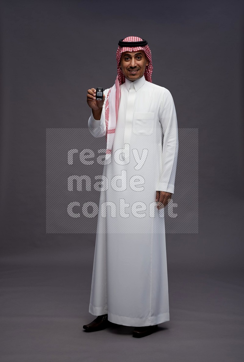 Saudi man wearing thob and shomag standing holding key car on gray background