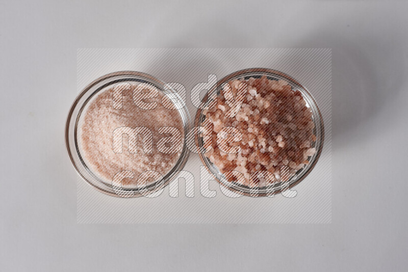 2 glass bowls one is filled with fine himalayan salt and the other with coarse himalayan salt on white background