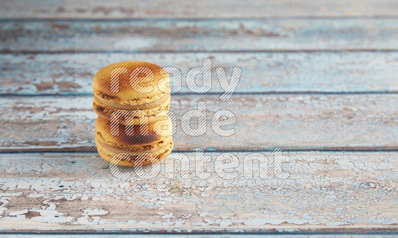 45º Shot of two Yellow Crème Brulée macarons on light blue wooden background