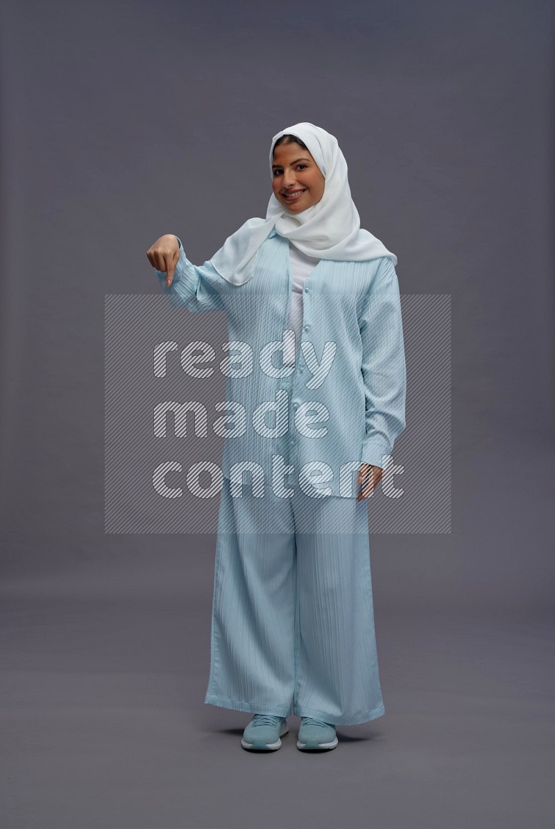 Saudi woman wearing hijab clothes standing interacting with the camera on gray background