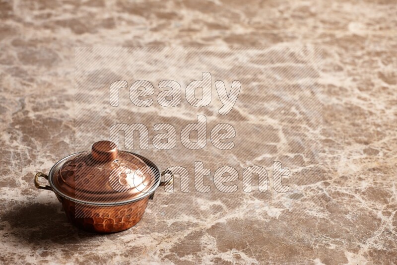 A small copper pot on beige marble background