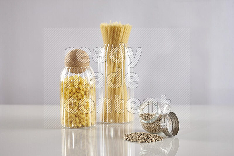 Raw pasta in glass jars with white peppers on light grey background