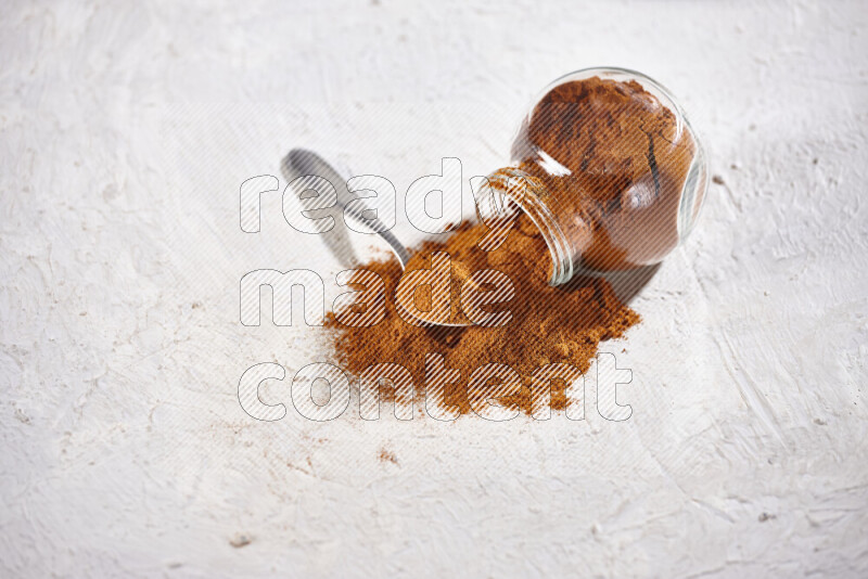 A glass jar full of ground paprika powder flipped with some spilling powder on white background