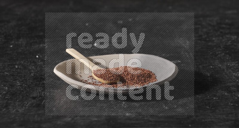 طبق فخار متعدد الألوان ممتلئ ببذور حب الرشاد وملعقة خشبية ممتلئة بالبذور على أرضية سوداء