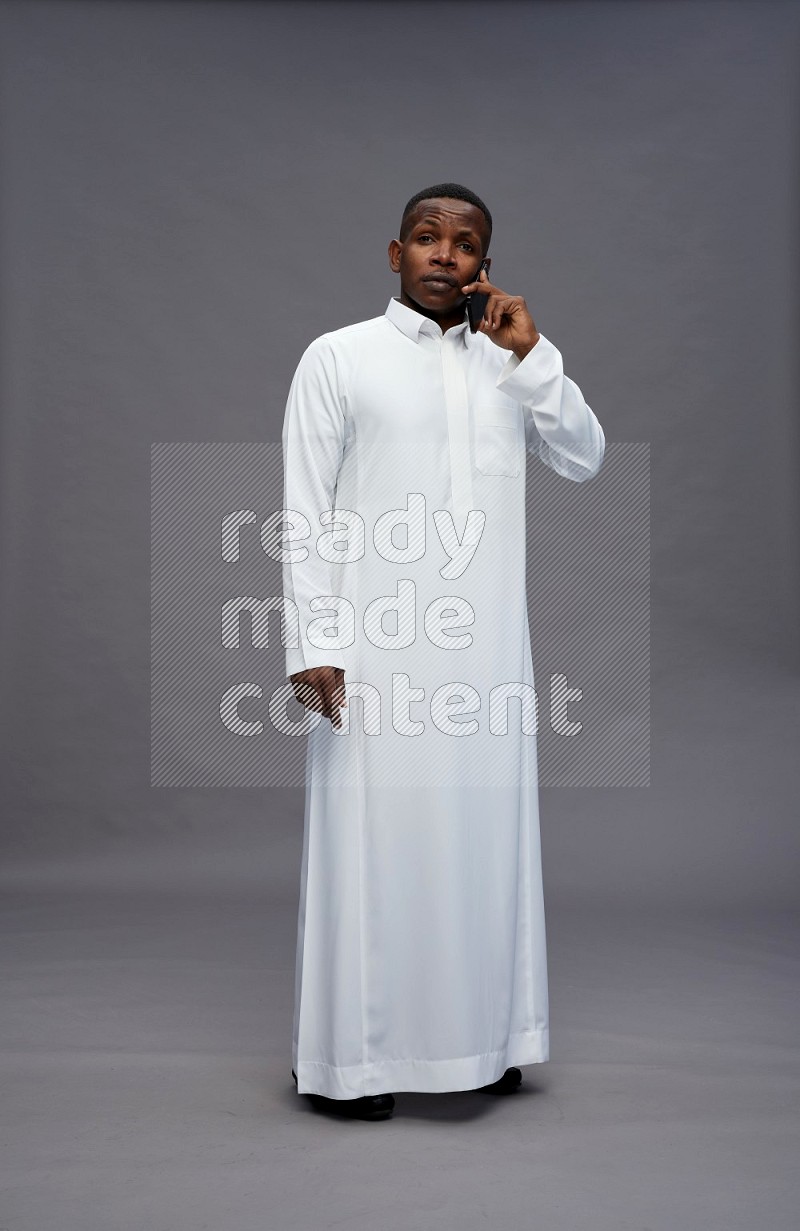 Saudi man wearing thob standing talking on phone on gray background