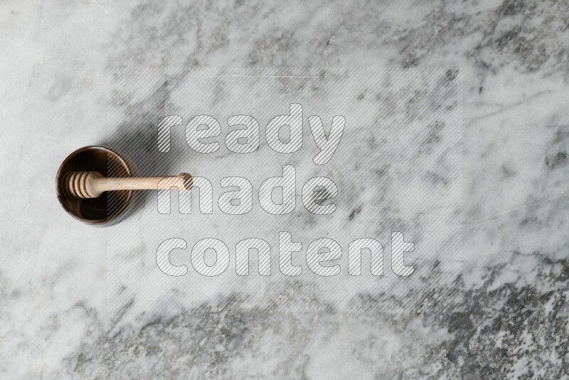 Brown pottery bowl with wooden honey dipper in it on grey marble background