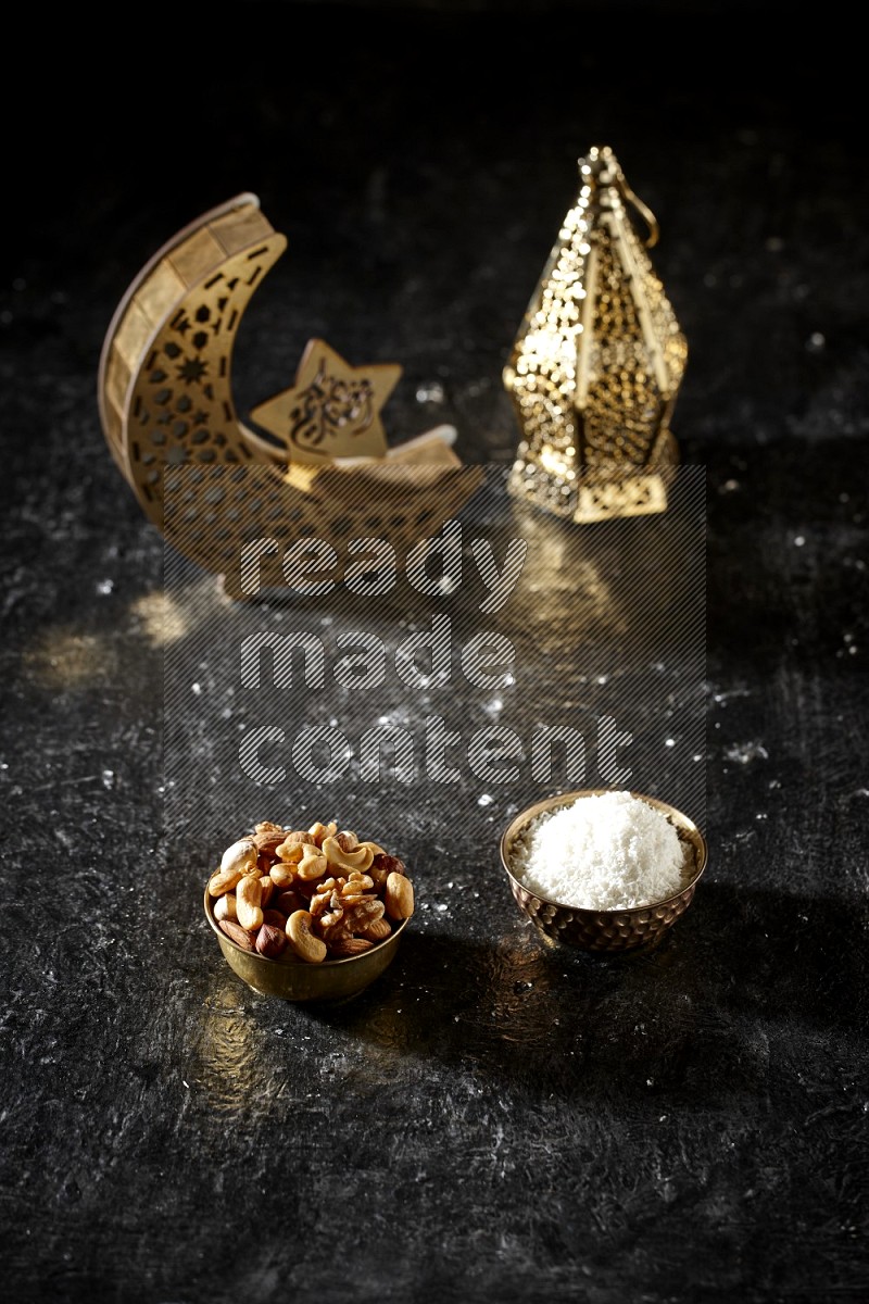 Nuts in a metal bowl with desiccated coconuts beside golden lanterns in a dark setup