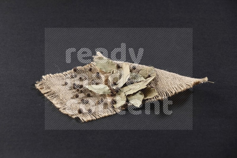 Dried bay leaves and allspice berries on a piece of burlap on black flooring