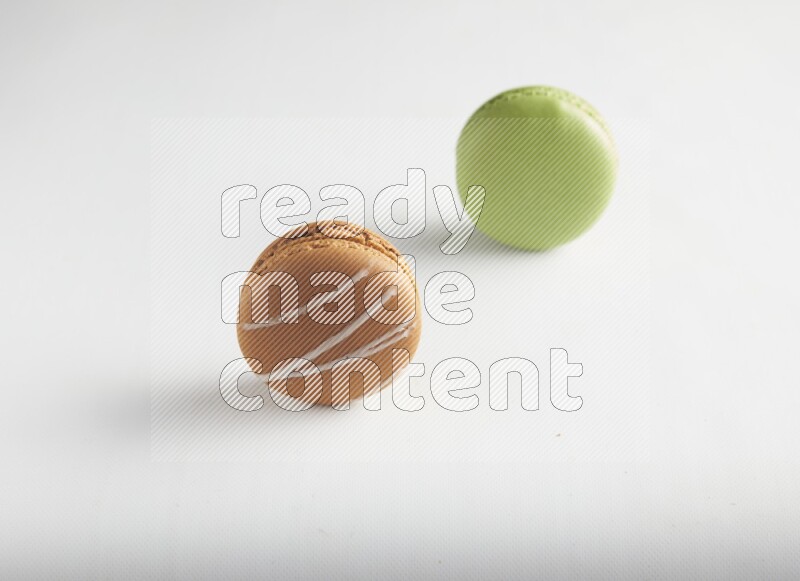 45º Shot of of two assorted Brown Irish Cream, and Green Pistachio macarons on white background