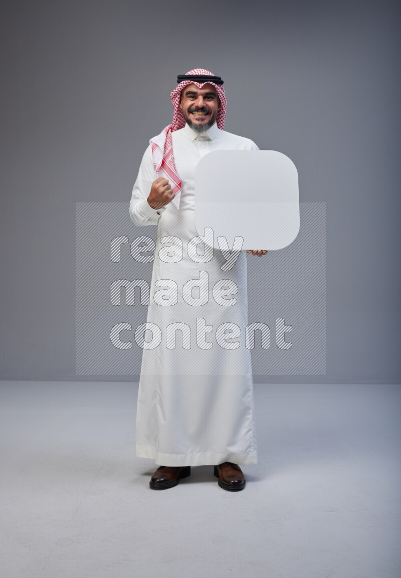 Saudi man Wearing Thob and red Shomag standing holding social media sign on Gray background