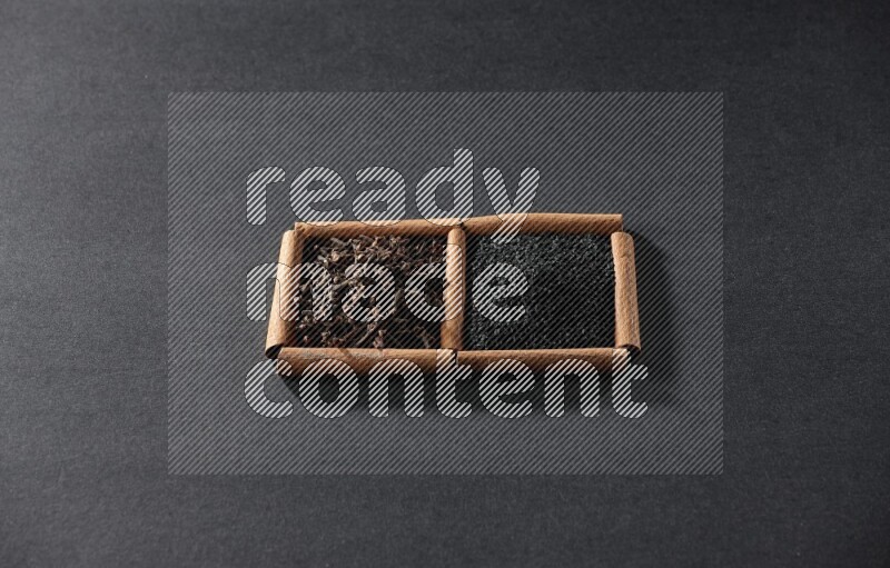 2 squares of cinnamon sticks full of black seeds and cloves on black flooring