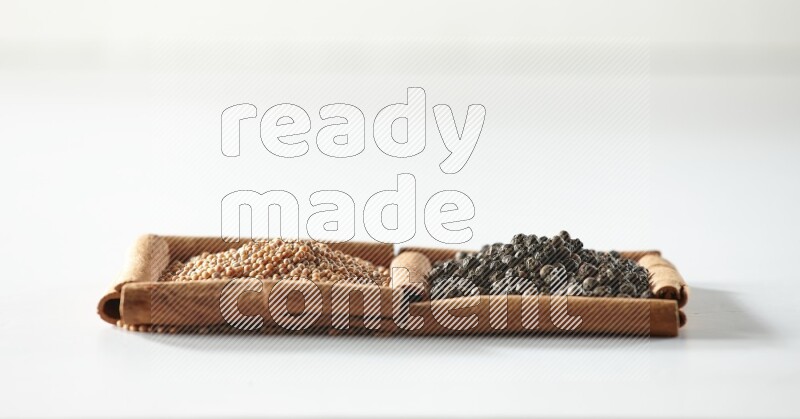 مربعان من أعواد القرفة ممتلئان بحبوب الخردل وحبوب الفلفل الأسود علي خلفية بيضاء